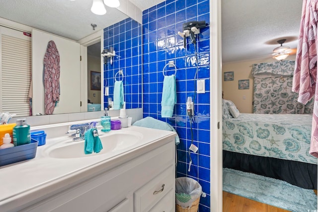 ensuite bathroom with vanity, a textured ceiling, ensuite bath, and tile walls