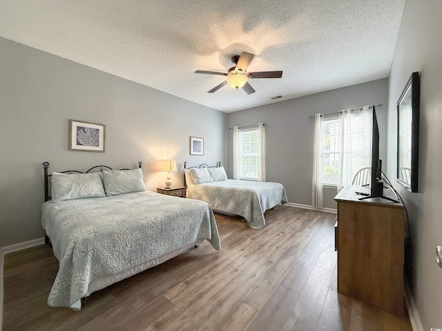bedroom featuring wood finished floors, a textured ceiling, visible vents, ceiling fan, and baseboards