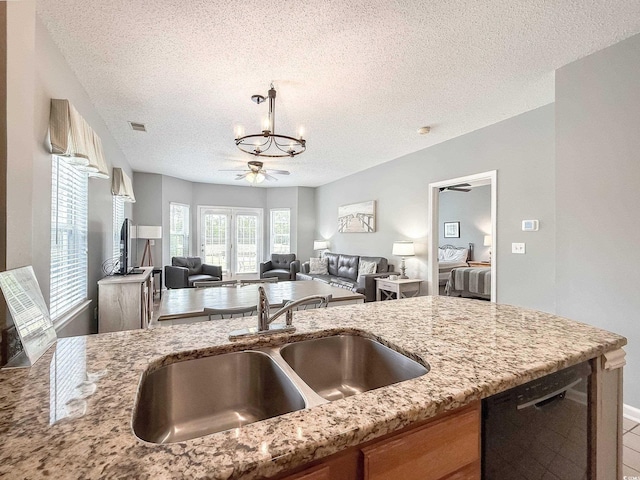 kitchen featuring light stone countertops, a textured ceiling, dishwasher, a sink, and ceiling fan with notable chandelier