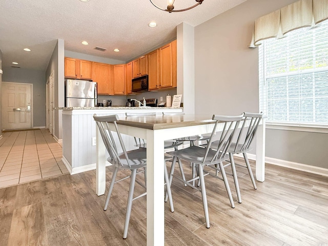 kitchen featuring freestanding refrigerator, visible vents, black microwave, light countertops, and light wood-type flooring