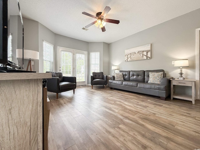 living room featuring ceiling fan, light wood finished floors, visible vents, and a textured ceiling
