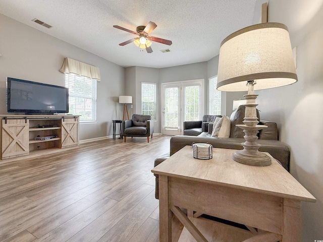 living room featuring wood finished floors, a textured ceiling, visible vents, a ceiling fan, and baseboards