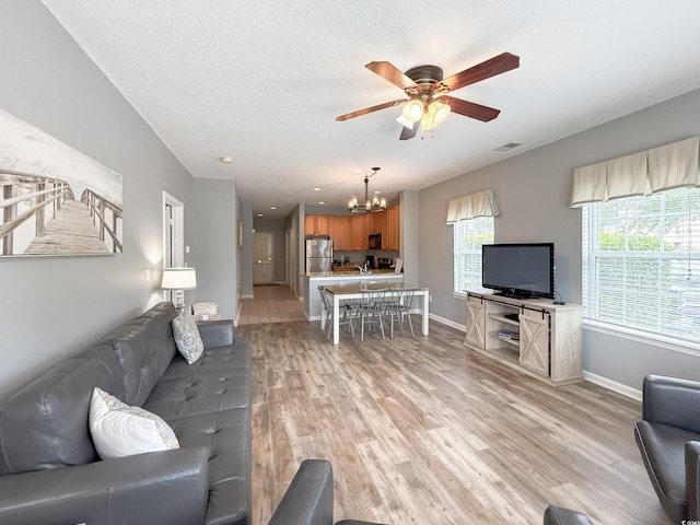 living room with ceiling fan with notable chandelier, a textured ceiling, visible vents, baseboards, and light wood-style floors
