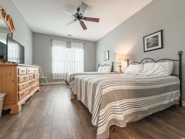 bedroom with a textured ceiling, baseboards, ceiling fan, visible vents, and wood finished floors