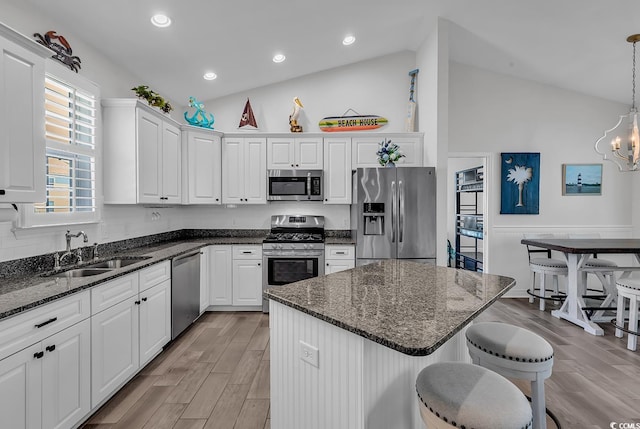kitchen featuring stainless steel appliances, a sink, lofted ceiling, white cabinets, and a kitchen breakfast bar