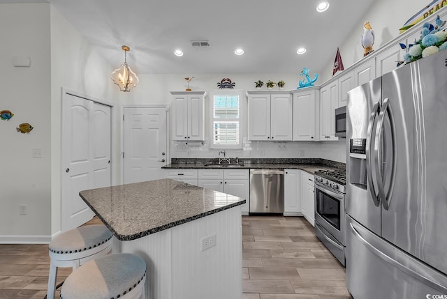 kitchen with stainless steel appliances, a breakfast bar area, a sink, white cabinetry, and wood finish floors