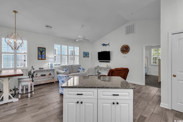 kitchen featuring wood tiled floors, a ceiling fan, dark stone countertops, white cabinetry, and a center island