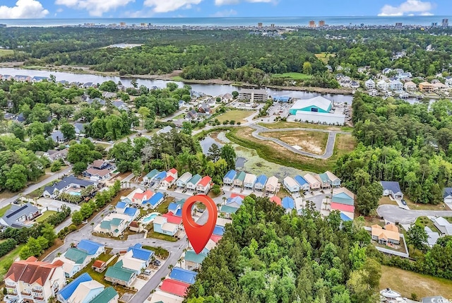 aerial view of property and surrounding area with a nearby body of water, a tree filled landscape, and nearby suburban area