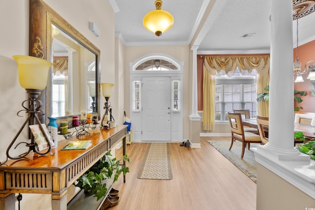 foyer entrance with ornate columns, wood finished floors, plenty of natural light, ornamental molding, and a textured ceiling