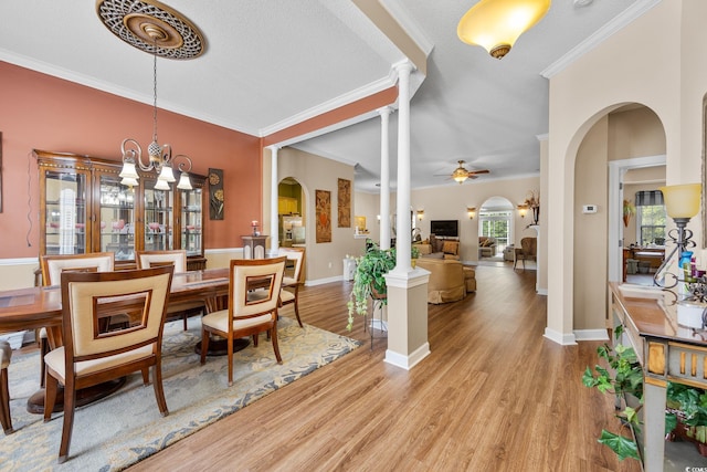 dining area with arched walkways, light wood-style floors, crown molding, a ceiling fan, and baseboards