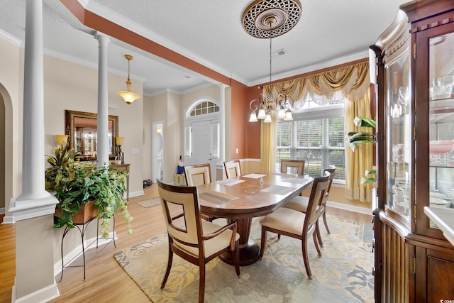 dining area with decorative columns, light wood-style flooring, ornamental molding, a textured ceiling, and baseboards