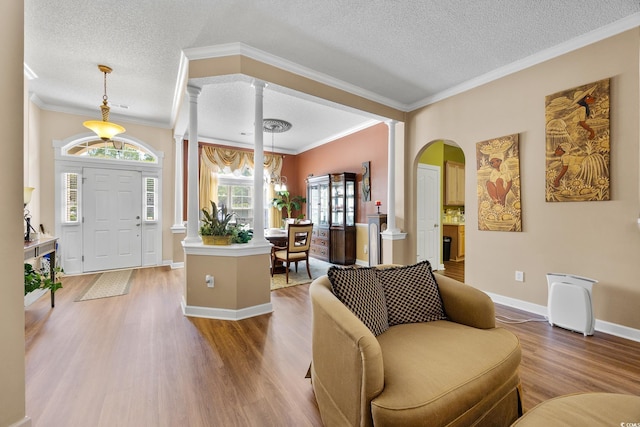 living area featuring ornate columns, wood finished floors, arched walkways, a textured ceiling, and baseboards