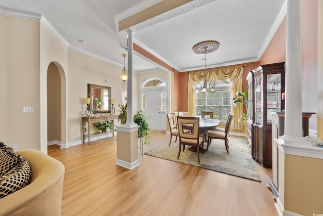 dining area with light wood-style flooring, a textured ceiling, ornate columns, a chandelier, and arched walkways