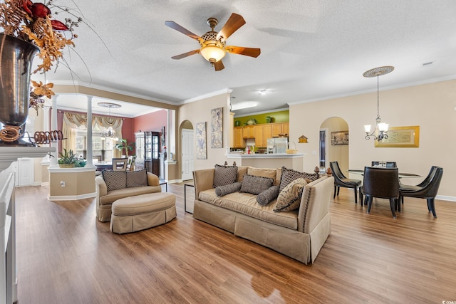 living area featuring arched walkways, a chandelier, light wood-style floors, ornamental molding, and a textured ceiling
