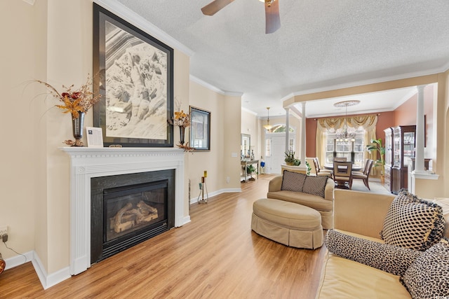 living area with wood finished floors, ornamental molding, a ceiling fan, a textured ceiling, and a glass covered fireplace