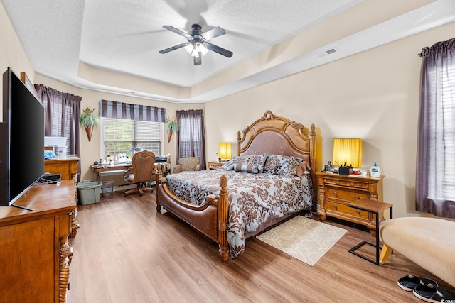 bedroom with wood finished floors, a raised ceiling, a ceiling fan, and a textured ceiling