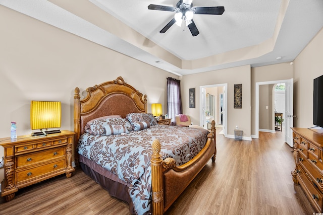bedroom featuring wood finished floors, a raised ceiling, baseboards, and a ceiling fan