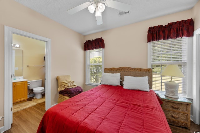 bedroom featuring wood finished floors, ensuite bath, and a ceiling fan
