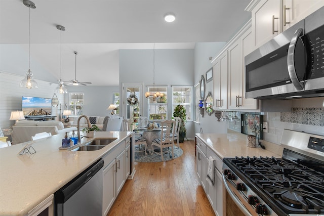 kitchen with stainless steel appliances, light wood-type flooring, a sink, and decorative light fixtures