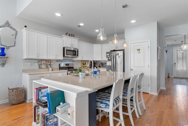 kitchen featuring a sink, stainless steel appliances, a breakfast bar area, light countertops, and white cabinets