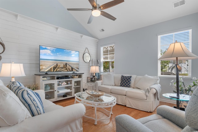 living room with a ceiling fan, wooden walls, visible vents, and wood finished floors