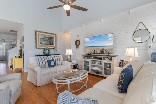 living room with wood finished floors, a towering ceiling, wooden walls, a ceiling fan, and baseboards