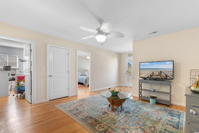 living room featuring baseboards, ceiling fan, light wood-style flooring, and visible vents