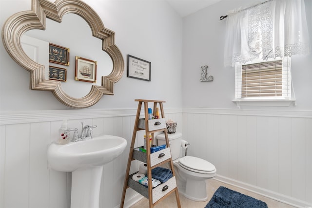 half bath with wainscoting, toilet, and a sink
