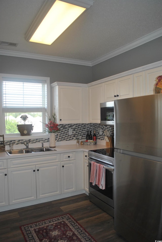 kitchen featuring stainless steel appliances, a sink, crown molding, white cabinetry, and tasteful backsplash