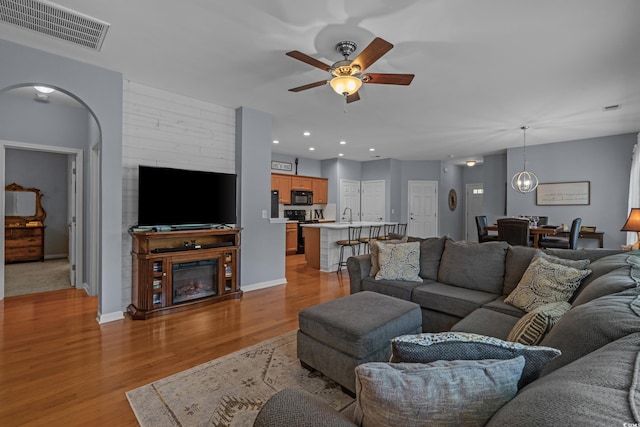 living room featuring ceiling fan, light wood finished floors, a glass covered fireplace, recessed lighting, and baseboards