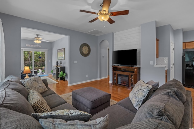 living area featuring ceiling fan, light wood-style flooring, arched walkways, and a glass covered fireplace