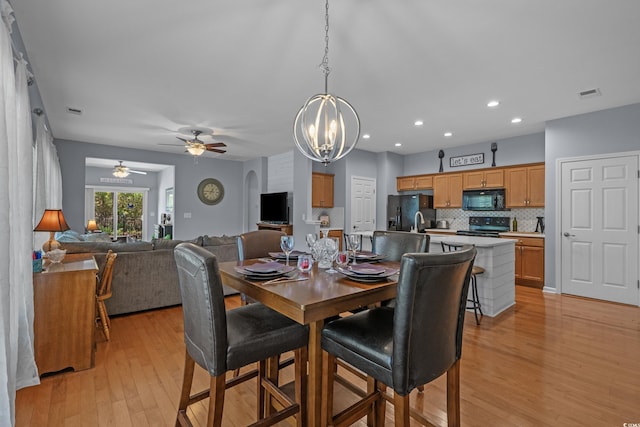 dining area featuring a chandelier, light wood-type flooring, a ceiling fan, recessed lighting, and arched walkways