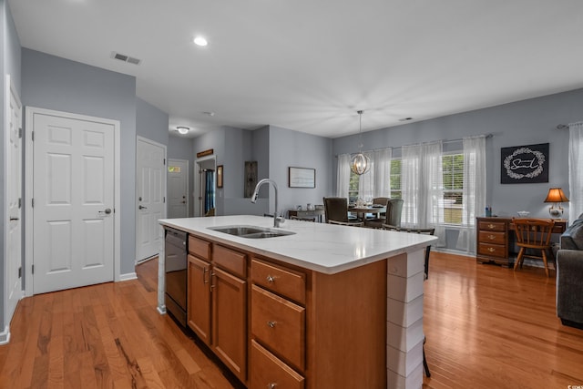 kitchen with a sink, dishwashing machine, light wood-style floors, brown cabinetry, and a kitchen island with sink