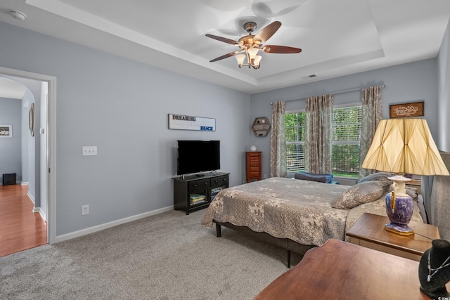 bedroom featuring a raised ceiling, arched walkways, carpet flooring, baseboards, and a ceiling fan
