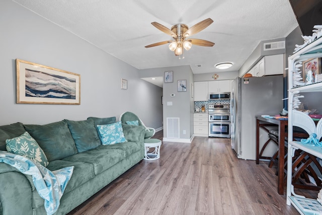 living room featuring baseboards, ceiling fan, visible vents, and wood finished floors