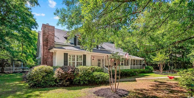 view of front of property with a front lawn, a sunroom, fence, and a chimney