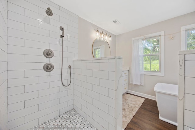 full bath featuring a tile shower, baseboards, visible vents, and wood finished floors