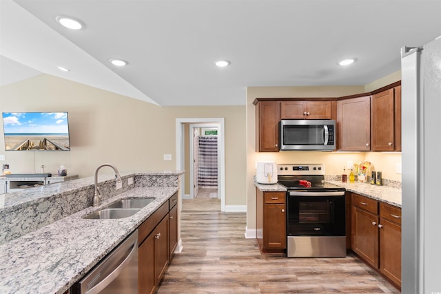 kitchen featuring light wood-style floors, stainless steel appliances, light stone countertops, and a sink