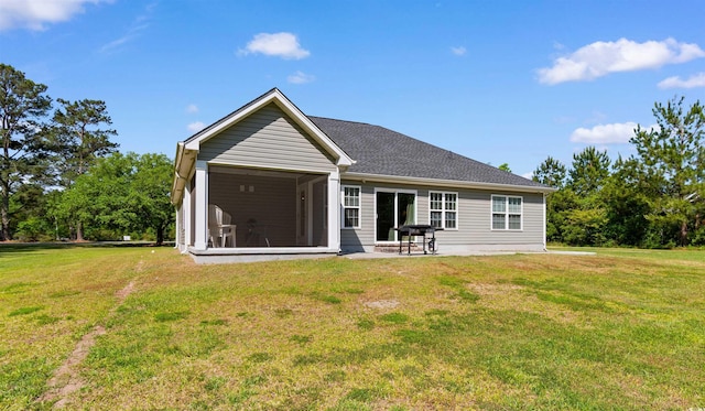 back of house with roof with shingles, a sunroom, and a lawn