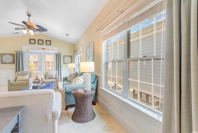 living area with french doors, ceiling fan, lofted ceiling, healthy amount of natural light, and wainscoting