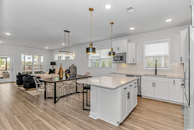 kitchen with light wood finished floors, a sink, stainless steel appliances, visible vents, and backsplash