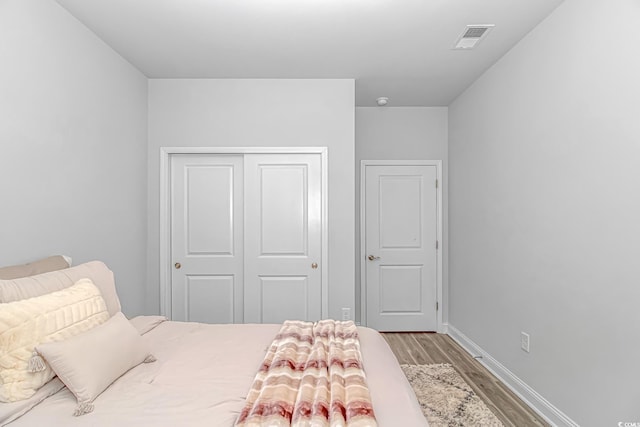 bedroom with a closet, baseboards, visible vents, and wood finished floors