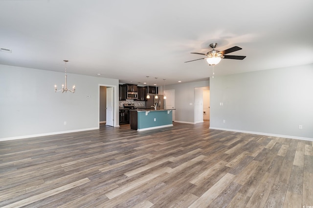 unfurnished living room featuring a ceiling fan, dark wood finished floors, a chandelier, and baseboards