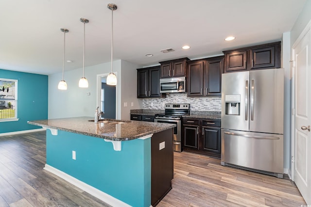 kitchen with stainless steel appliances, a sink, a breakfast bar, light wood-style floors, and decorative backsplash