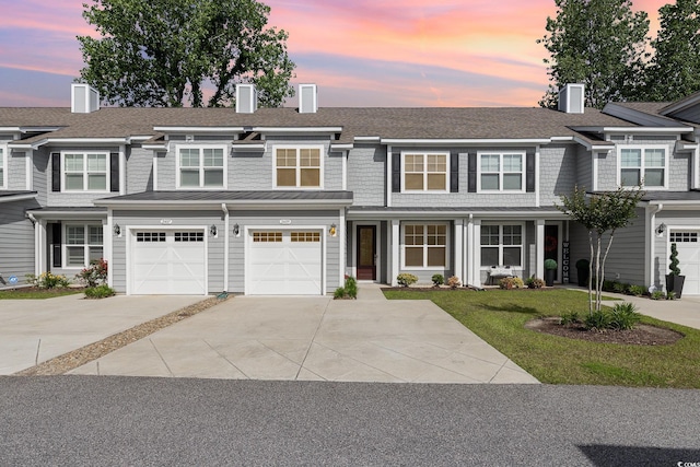 shingle-style home with driveway, a chimney, an attached garage, and a front lawn