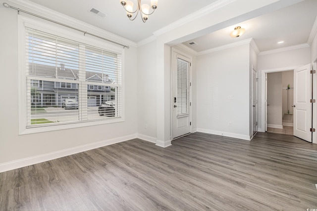 spare room featuring a chandelier, healthy amount of natural light, wood finished floors, baseboards, and crown molding