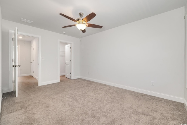 unfurnished bedroom featuring light colored carpet, a spacious closet, baseboards, ceiling fan, and a closet