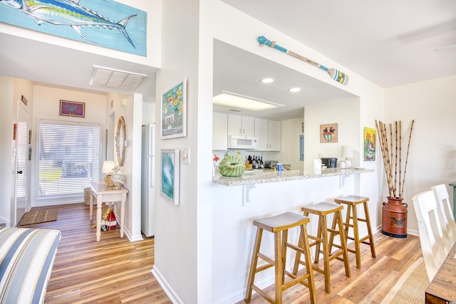 kitchen with white appliances, light wood finished floors, a breakfast bar area, baseboards, and recessed lighting