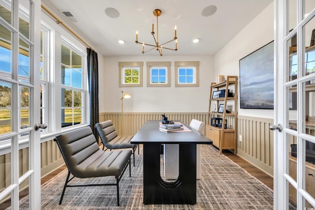 dining area with french doors, wood finished floors, visible vents, wainscoting, and a chandelier