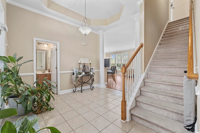 stairway with baseboards, decorative columns, tile patterned flooring, crown molding, and a raised ceiling